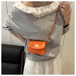Detail of orange mini crossbody bag with white butterfly buckle on casual outfit
