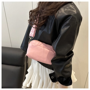 Detail of pink crossbody bag featuring adjustable wave pattern wide strap and gold hardware