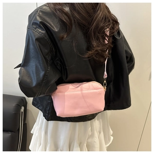 Detail of pink PU leather crossbody bag with gold hardware worn over a black leather jacket