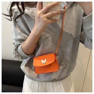 Detailed view of an orange mini crossbody bag featuring a delicate white butterfly ornament