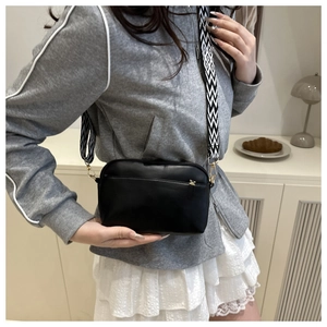 Detail of black crossbody bag with wide geometric pattern strap shown on a model
