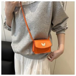 Detail of a mini orange crossbody bag with white butterfly buckle worn by a model