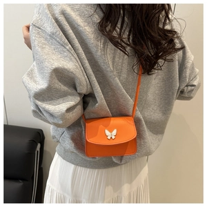 Detail of orange mini crossbody bag with a white butterfly ornament on smooth leather