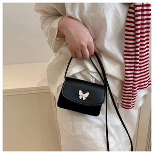 Detail of a black mini square bag with butterfly metal buckle and slim strap