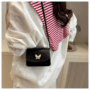 Close-up of black leather crossbody bag featuring an elegant white butterfly buckle