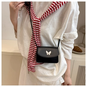 Close-up of black leather crossbody bag with white butterfly metal buckle on a model