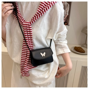 Detail of a black mini crossbody bag featuring a silver butterfly buckle on white shirt