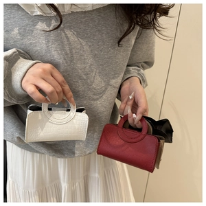 Close-up of a white mini handbag with crocodile texture and unique circular metal handle