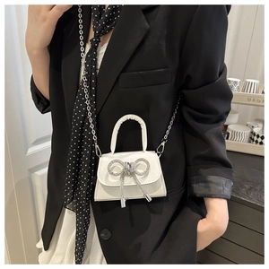 Detail van witte mini crossbody tas met een sprankelende strass strik en zilveren ketting