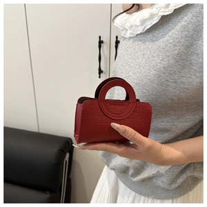 Detail of red croc-embossed mini handbag with unique circular handles in a daily setting