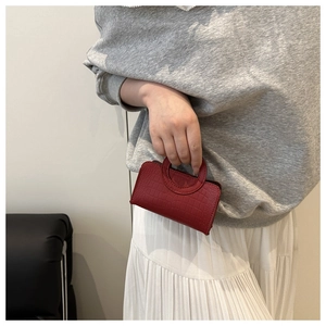 Detailed close-up of a bright red mini crocodile-patterned handbag with round handle