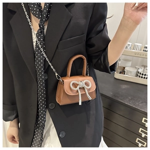 Détail d'un mini sac marron à nœud avec boucle en strass et chaîne argentée sur modèle
