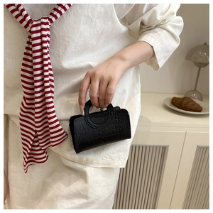 Detail of a black crocodile-pattern mini handbag with a round handle held by a model