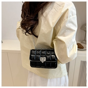 Model wearing a black quilted leather mini bag with silver chain strap in home setting