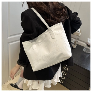 Detail of white tote bag featuring embossed crocodile pattern and slim shoulder straps