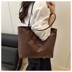 Detail of a large brown tote bag featuring a textured crocodile pattern and shoulder strap