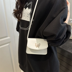 Mini white crossbody bag with elegant butterfly buckle on a black hoodie background