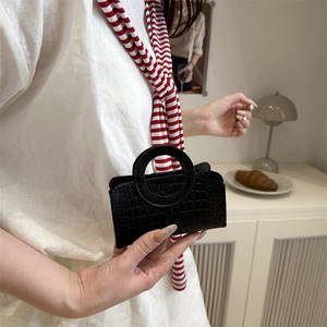 Minimalist black handbag with crocodile pattern and round handle for elegant styling