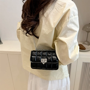 Glossy black quilted crossbody bag with silver chain and metal lock on a female model