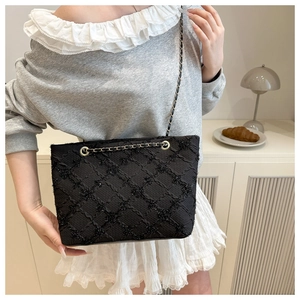 Detail of black quilted chain bag with shimmering metallic fibers and gold hardware