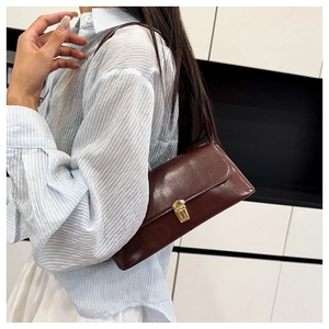 Detail shot of a vintage deep burgundy baguette bag with gold metal buckle on a model