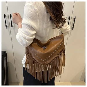 Brown tassel shoulder bag with metallic studs and cross detail worn by a model