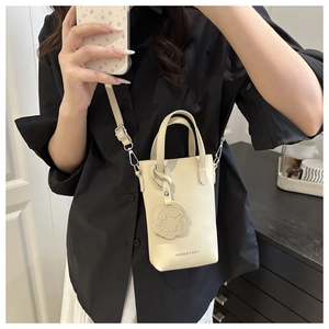 Close-up of cream PU crossbody bucket bag with dog pendant and fashion text detail