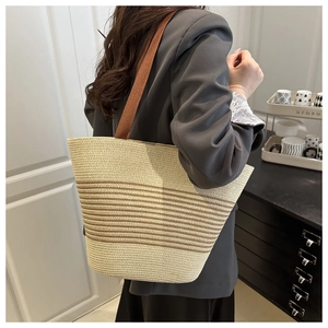Detail of a beige woven tote bag with brown stripes and wide fabric shoulder strap