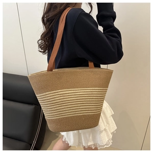 Detail of large woven straw tote bag with brown stripes and orange shoulder strap