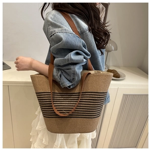 Close-up of woven straw tote bag with black stripes and brown fabric handles