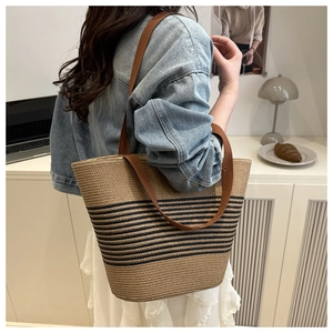 Detail of hand-woven straw bucket bag with black stripes and brown strap on a model