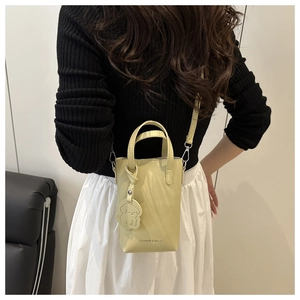 Detail of yellow lychee pattern mini bucket bag with dog charm on black leather sofa