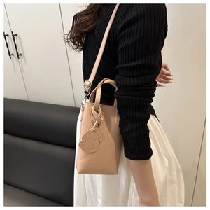 Vue latérale du sac seau beige en cuir avec breloque chien et fine bandoulière