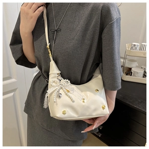 Close-up of white glossy hobo bag with gold floral studs and oversized lace pearl bow