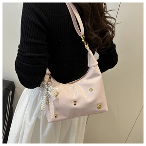 Pink glossy shoulder bag with metallic bone studs and a pearl heart charm on a model