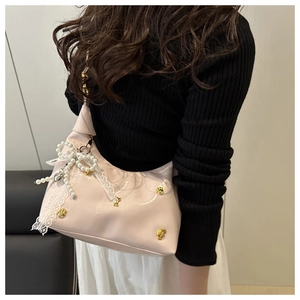 Detail of light pink glossy underarm bag with lace bow, pearls, and gold paw studs