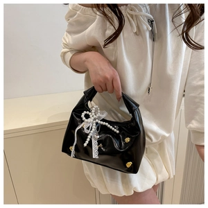 Close-up of black glossy handbag featuring gold studs, white lace bow, and pearl charm