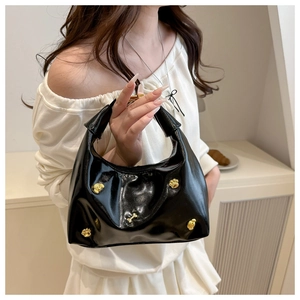 Detail of black patent leather tote bag with 3D gold flower studs and top handle