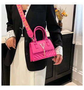 Detail of fuchsia crossbody bag featuring a golden V logo with a stylish patterned wide strap