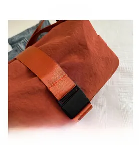 Detail of durable orange fabric with nylon strap and black plastic buckle on crossbody bag