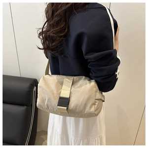 Detail of adjustable strap with black buckle on beige nylon crossbody bag shown on model