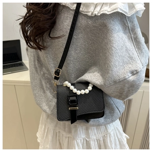 Detail of black woven crossbody bag featuring decorative white pearl handle and gold hardware