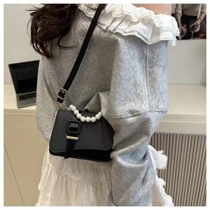 Detail of elegant black crossbody bag featuring pearl handle and woven texture leather