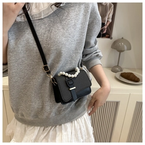 Detail of black crossbody bag featuring textured embroidery and white pearl chain handle