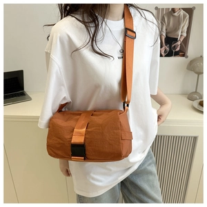 Detail view of the orange crossbody bag with wide strap and buckle closure in office setting