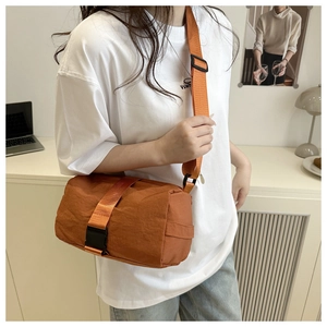 Close-up of orange nylon crossbody bag with wide shoulder strap and plastic buckle detail