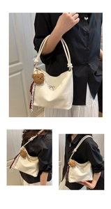 Detailansicht der cremefarbenen Hobo-Tasche mit Metallschleife und Bärenanhänger
