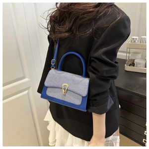 Detail of blue denim patchwork handbag with golden horseshoe buckle on black suit model