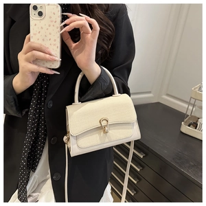 Detail of cream leather handbag with gold horseshoe buckle on dark wood table