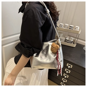 Detail of silver metallic shoulder bag with metal bow buckle and plush bear pendant